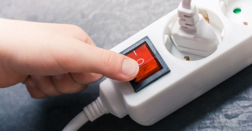 Persona apagando regleta de enchufes para evitar consumo innecesario y reducir consumo de electricidad