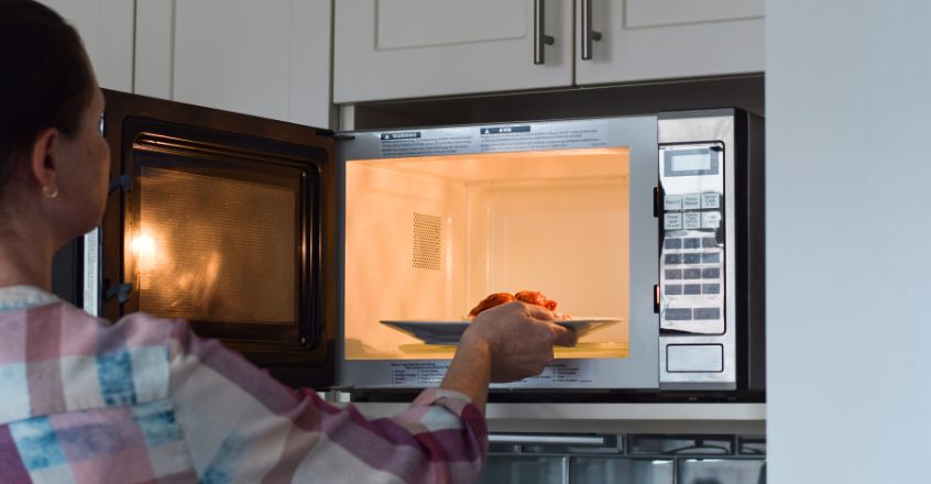 Mujer usando microondas en lugar del horno como opción eficiente para reducir consumo de electricidad