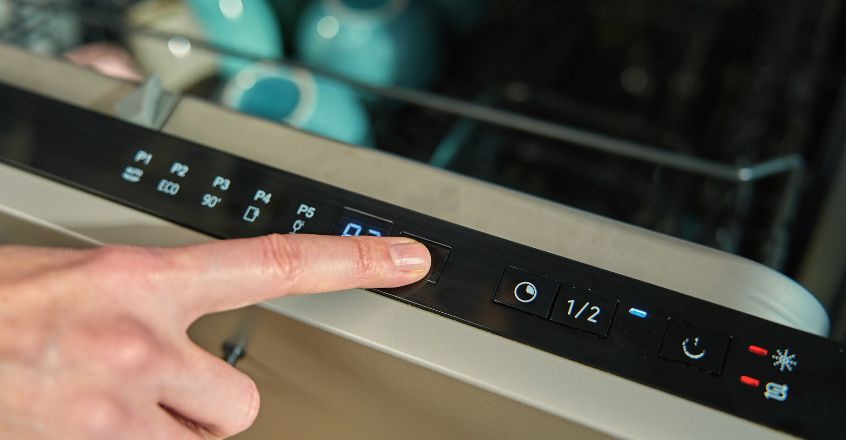 Mano encendiendo lavavajillas eficiente con programa eco para reducir consumo de electricidad