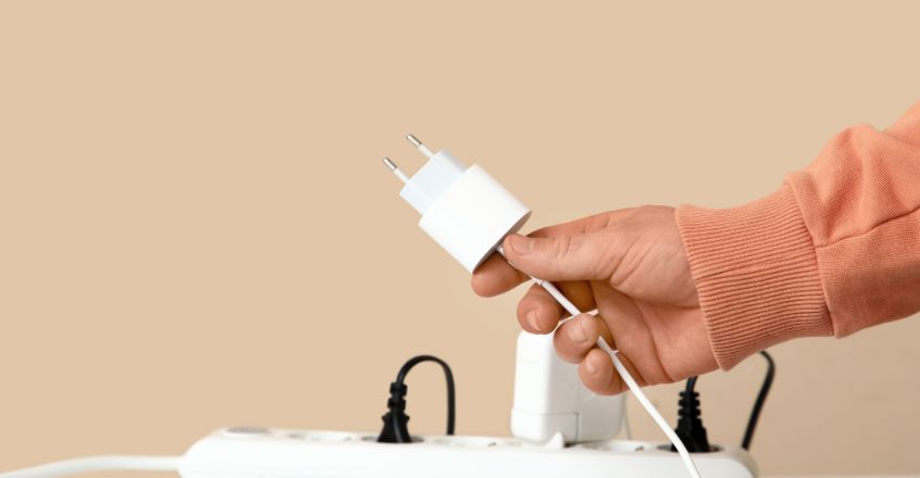 Persona desenchufando cargador de regleta para evitar gasto fantasma y reducir consumo de electricidad